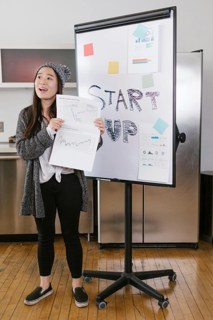 A young woman gives a startup presentation with charts and graphs on a flipchart.