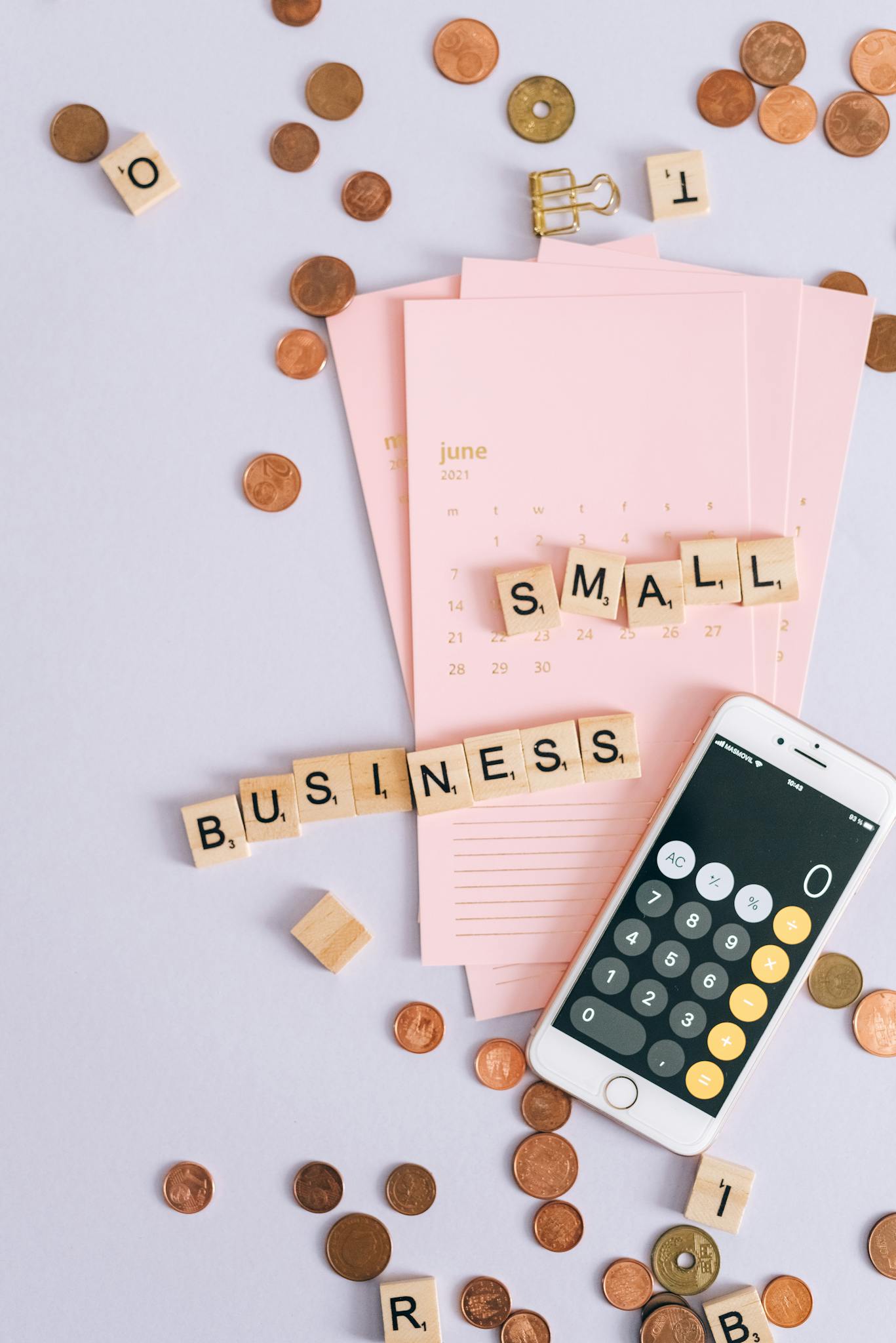Flat lay of small business essentials with calculator, calendar, coins, and tiles.