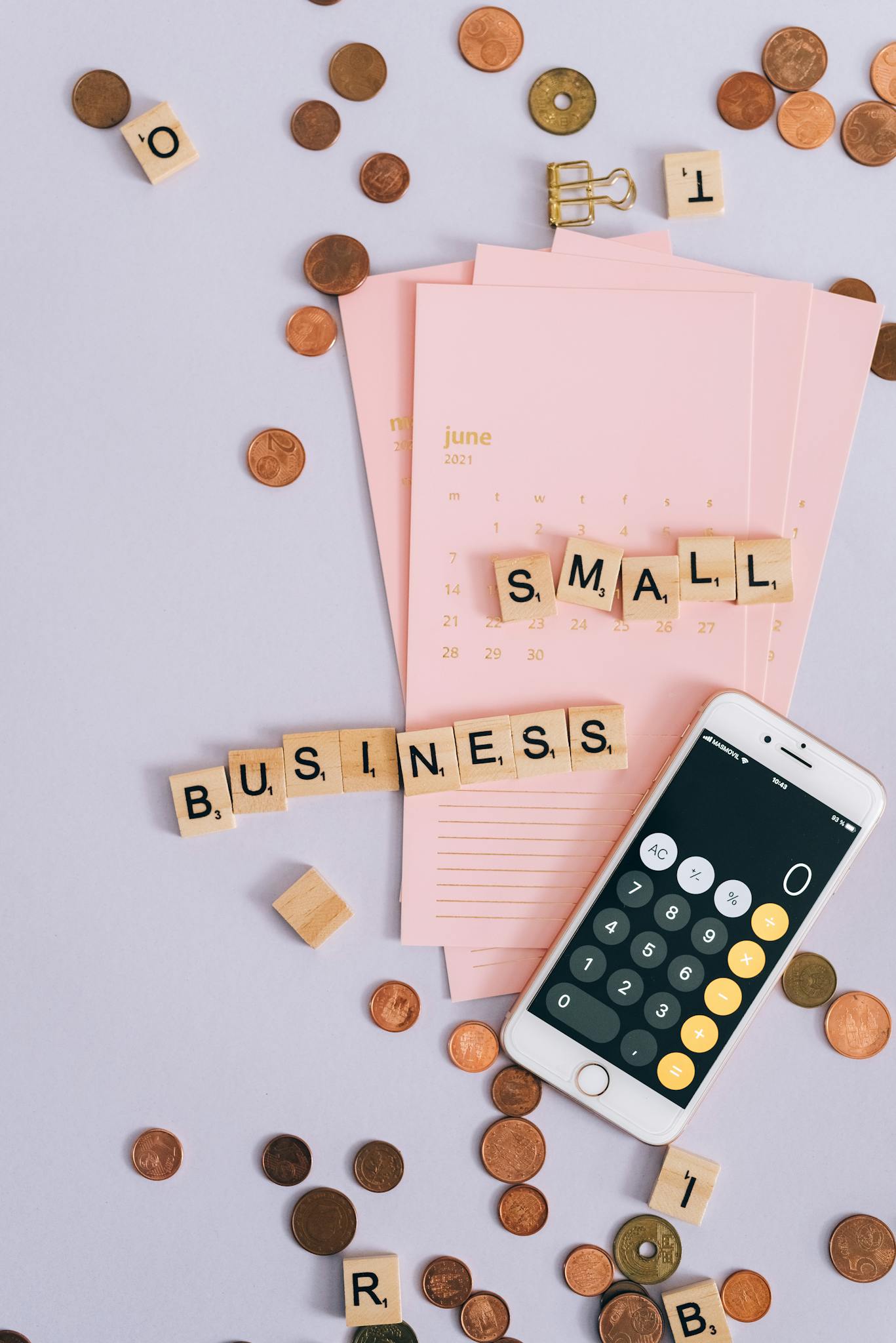 Flat lay with coins, smartphone, and 'SMALL BUSINESS' tiles on a planner.